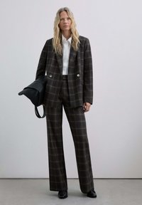 Traje de cuadros en tonos oscuros que incluye un blazer de doble botonadura y pantalones de pierna ancha, combinado con una camisa blanca y un bolso negro.