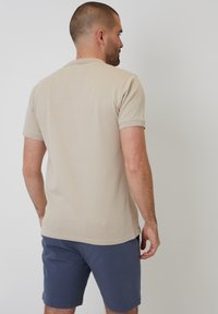 Bežové polo tričko s krátkými rukávy, strukturovaný design, kulatý límec, v kombinaci s tmavě modrými šortkami, pohled zezadu.