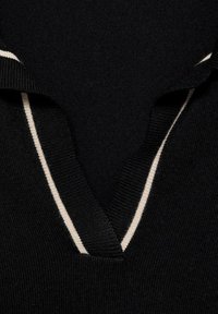 Schwarzer Strickpullover mit V-Ausschnitt, der einen weißen gestreiften Saum am Kragen aufweist. Strukturiertes Material mit glatter Oberfläche.