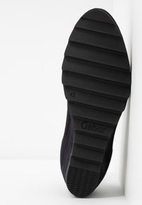 Semelle en caoutchouc noire avec texture striée. Marque "Gabor" visible. Accompagnée d'un dessus en tissu foncé et doux. Conçue pour le confort.