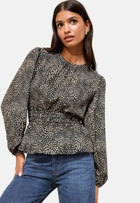 Blusa nera con motivo a macchie crema, scollatura arricciata, vita elasticizzata e maniche ampia. Abbinata a jeans in denim blu.