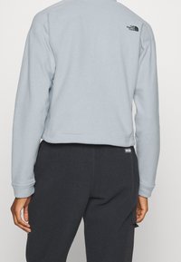 Jasnoniebieski skrócony sweatshirt z długimi rękawami, z czarnym logo na plecach. W połączeniu z ciemnymi spodniami z polaru.