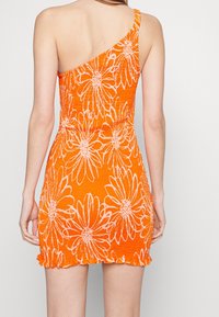 Oranžové šaty s asymetrickým designem na jednom rameni, s bílými vzory sedmikrásek a volánkovými detaily na spodním okraji. Texturovaný materiál se sklady.