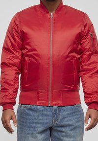 Giacca bomber rossa realizzata in materiale lucido e morbido; presenta una zip frontale, un colletto a costine e tasche laterali. Polsini e vita testurizzati.