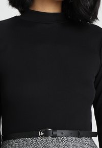 Svart randig långärmad topp med hög halsringning, tillsammans med en kjol i hounds-tooth-mönster och ett smalt svart bälte i midjan.