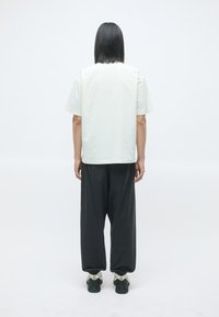 Lysfarget t-skjorte med korte ermer kombinert med løstsittende mørke bukser og svarte joggesko. Enkelt design med en minimalistisk estetikk.