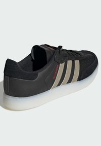 Czarny sneaker z trzema beżowymi paskami, zamszowa i syntetyczna cholewka, perforowany czubek, biała gumowa podeszwa oraz czerwone logo z boku.