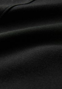 Tela negra con una textura suave y mate, cayendo de manera natural con pliegues sutiles y una superficie lisa, mostrando suavidad y flexibilidad.