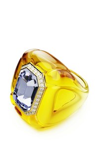 Gul hartsring med en stor oktagonal ljusblå ädelsten, omgiven av en rad klara stenar, med en slät och glansig yta.