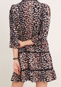 Robe à imprimé léopard en marron, noir et crème, avec des manches longues, un ourlet volanté et des accents noirs à la taille. Texture de tissu douce.