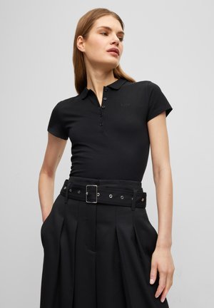 Polo shirt nera a maniche corte con un design classico con colletto e bottone; abbinata a pantaloni neri a vita alta e cintura.
