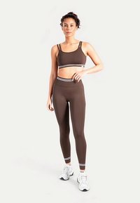 Brassière de sport marron et leggings assortis avec des bandes blanches en accent. Le tissu semble texturé et ajusté, avec une taille haute et des bretelles.