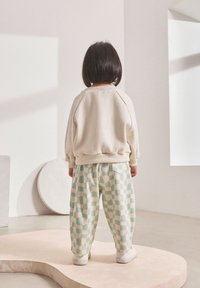 Cremefarbener Fleece-Pullover mit gerippten Bündchen, kombiniert mit mintgrünen karierten Hosen, Rückansicht, mit lockerem Sitz und weicher Textur.