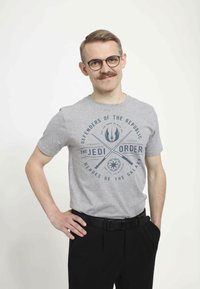Šedé bavlněné tričko s krátkými rukávy a kulatým výstřihem, na kterém je modrý grafický text a symboly ze Star Wars. Černé kalhoty.