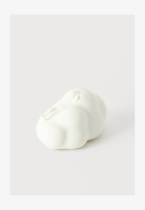Objet blanc en forme de nuage avec une petite figure humaine couchée sculptée dessus, sur un fond clair uni.