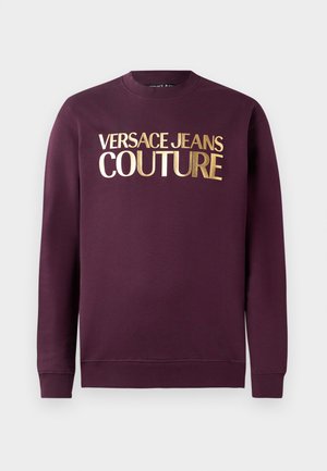 Burgundinje sweatshirt s okruglim izrezom, sa zlatnim metalnim tekstom "VERSACE JEANS COUTURE" na prednjoj strani. Glatka tekstura, rebrasti rubovi.