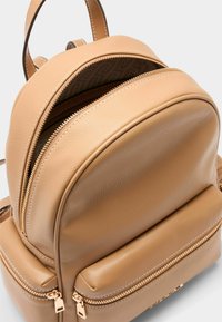 Mochila de cuero color canela con diseño redondeado. Cuenta con dos compartimentos con cremallera, herrajes en tono dorado y un acabado texturizado.