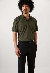 Nike kortermet polo skjorte i olivengrønn med et teksturert geometrisk mønster, kombinert med svarte bukser og et svart belte.
