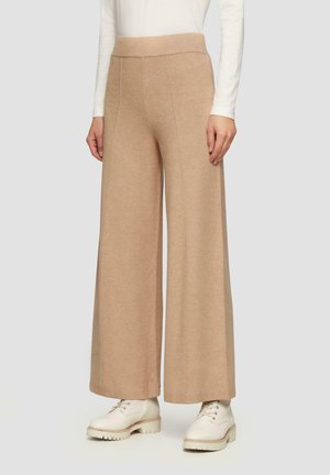 Beige weite Hosen mit einem hohen elastischen Bund, weicher Textur und sichtbaren Nähten, kombiniert mit hellen Schnürschuhen.