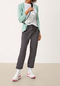 Ljus mintfärgad cardigan över en vit t-shirt, grå joggers och vita sneakers med rosa detaljer. Metallisk silverfärgad axelremsväska.