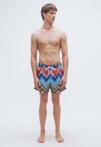 Μαγιό σορτς με ζιγκ ζαγκ μοτίβο σε κόκκινο, μπλε, πράσινο και μαύρο. Κατασκευασμένα από ελαφρύ ύφασμα με ελαστική μέση με κορδόνι.