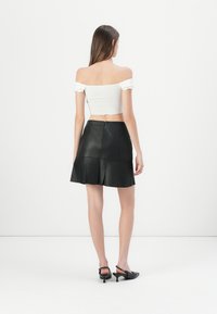 Balts off-the-shoulder top, kombinēts ar melnu ādas A-līnijas svārku. Svārkiem ir redzams rāvējslēdzis un slāņaina dizaina struktūra.