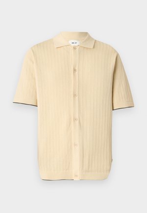 Μπεζ κοντομάνικο πλεκτό πόλο με κουμπιά εμπρός και διακριτικά κάθετα σχέδια, με γιακά και μαύρο περίγραμμα στις άκρες των μανικιών.