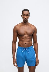 Μπλε μαγιό με ελαστική μέση και ρυθμιζόμενο κορδόνι. Κατασκευασμένο από ελαφρύ ύφασμα, με ομαλή υφή και χωρίς ορατά σχέδια.