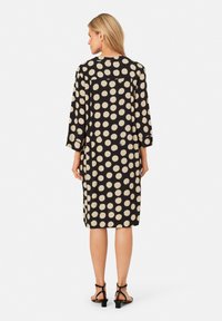 Schwarzes Kurzarmkleid mit großen beigen Punkten, lockere Passform, knielang, mit rundem Halsausschnitt und seitlichen Schlitzen.