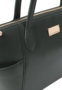 Sac à main en cuir vert foncé avec une texture lisse, fermeture à glissière et finitions en or rose. Il comporte deux poignées et une poche avant.