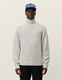 Hellgrauer, gestrickter Rollkragenpullover mit geripptem Saum, der dunkle Flecken aufweist. Kombiniert mit einer blauen Mütze, die weißen Text zeigt.