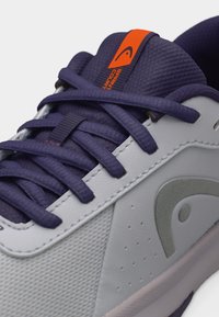 Hästi lähedalt pildistatud halli ja tumesinise spordijalatsiga, tumesiniste paeltega, oranži sildiga keelel ja halli logoga külgpaneelil.