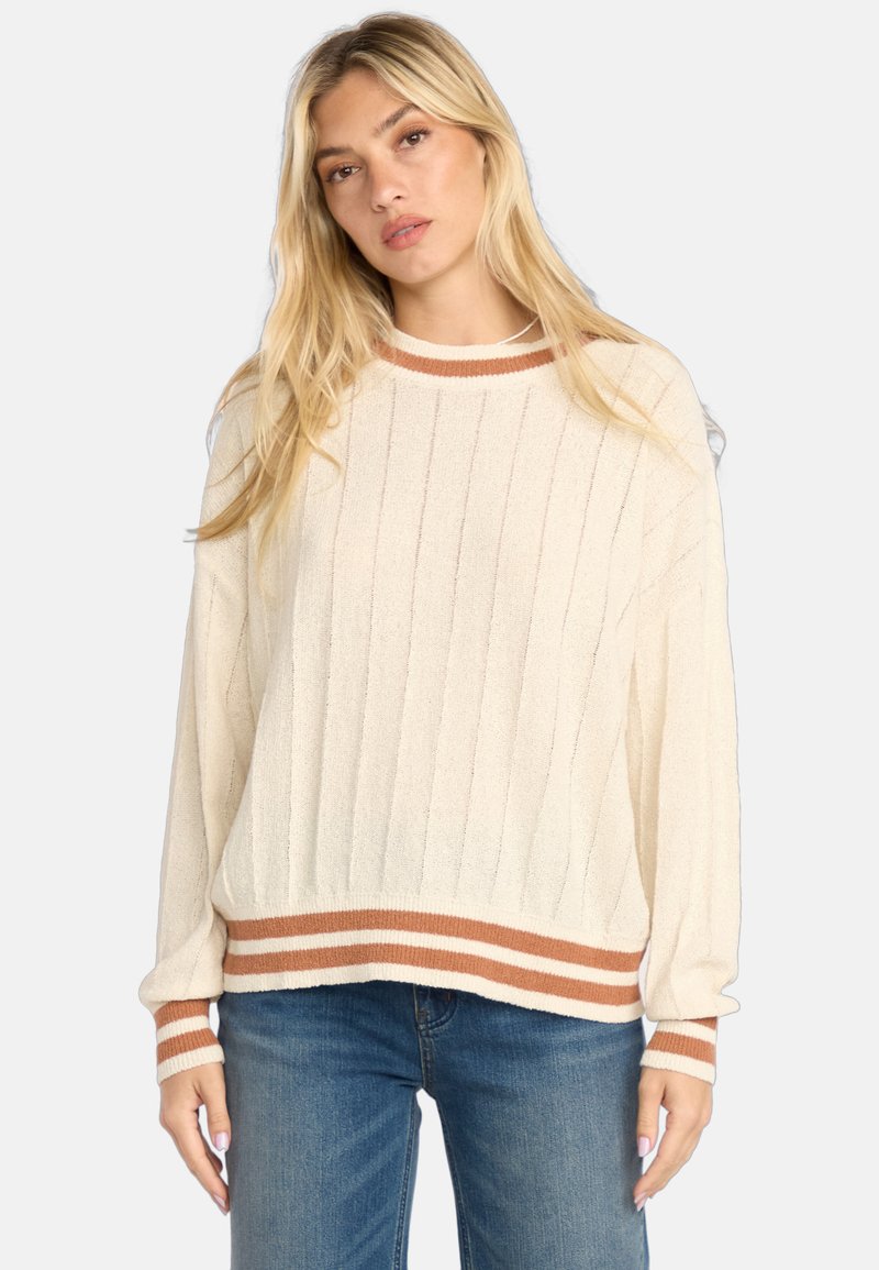 Pull rayé crème avec un tissu texturé, présentant un ourlet et des poignets marron en côtes, et un design à coupe décontractée. Associé à un jean bleu.