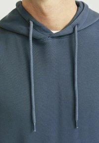 Sudadera con capucha en azul oscuro, con un tejido texturizado, cordones y un ajuste relajado. Detalles de costura visibles a lo largo del cuello.