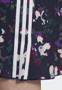 Námořnická sukně z látky s duhovým květinovým vzorem, která má tři vertikální bílé pruhy na jedné straně a surový lem.