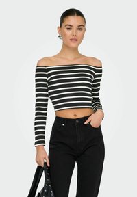 Sort og hvid stribet off-the-shoulder crop top med lange ærmer, ribbet tekstur, kombineret med højtaljede sorte jeans og en sort taske.
