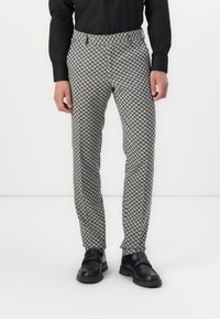 Black and white houndstooth patterned trousers with a tailored fit, featuring a smooth texture and a discrete pocket at the waistband.