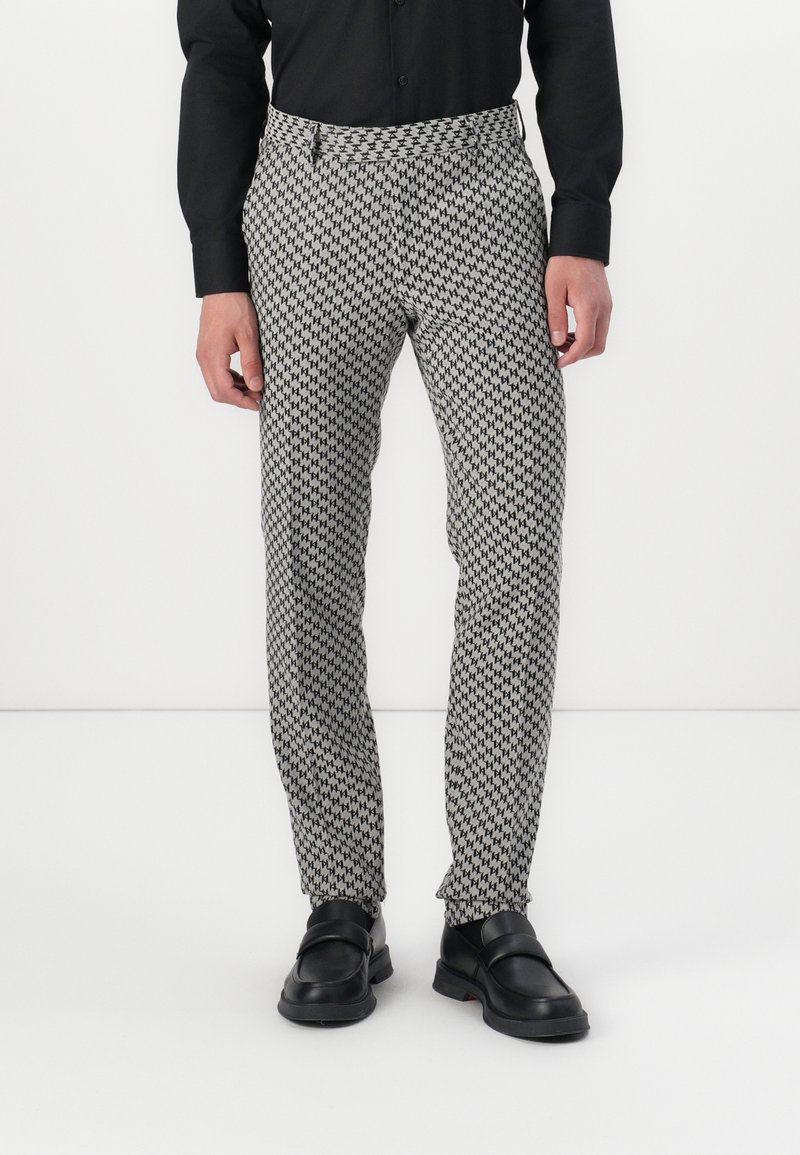 Black and white houndstooth patterned trousers with a tailored fit, featuring a smooth texture and a discrete pocket at the waistband.