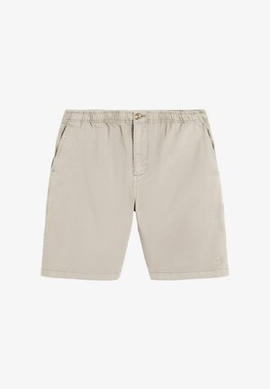 Pantalones cortos beige con cintura elástica con cierre de botón, bolsillos laterales y un pequeño logo de calavera y huesos cruzados cerca del dobladillo inferior en la pierna derecha.