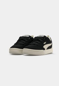 Black sneakers with a textured upper, white Puma logo, and cream rubber sole. Features rounded toe and flat laces.