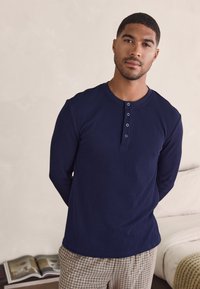 Navy long-sleeved ribbed t-shirt with a round neckline and five-button placket, showcased worn with beige checkered pants.