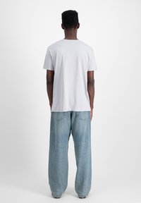 Balta kokvilnas T-kreklu ar brīvu piegriezumu, apaļu kaklu un īsām piedurknēm, apvienota ar gaiši ziliem, platām kājām džinsiem.