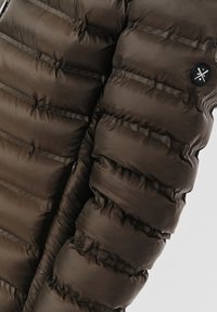 Kurtka puchowa w ciemnobrązowym kolorze, z pikowanymi sekcjami, gładką teksturą oraz czarnym okrągłym logo na rękawie. Widoczny detal z zamkiem.