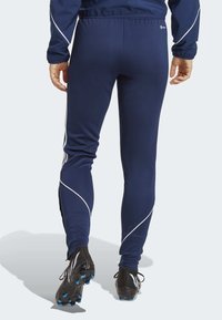 Marineblauwe sportbroek met witte piping, aangesloten ontwerp, rekbaar materiaal en zwarte sportschoenen met blauwe accenten, getoond vanaf de achterkant.