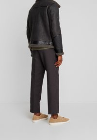 Giubbotto di pelle nera con colletto in pelliccia, maglione grigio a trama, pantaloni scuri a fantasia e sneakers beige chiaro.