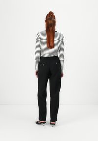 Pantalones negros de corte recto, con bolsillos traseros y botones decorativos, combinados con una camisa de manga larga a rayas blancas y negras.