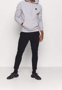 Grå huvtröja med framficka och svart logotyp, ihop med svarta smalnande sweatpants och svarta träningsskor.