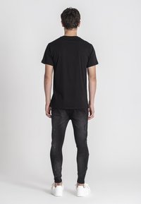 Čierne tričko s krátkym rukávom a okrúhlym výstrihom, kombinované s tesne priliehavými čiernymi džínami. Model má na sebe biele tenisky.