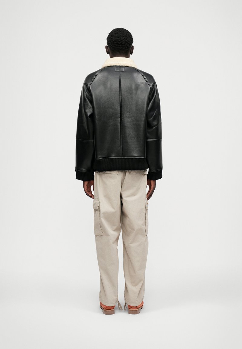 Schwarze lederne Jacke mit einem crèmefarbenen Lammfellkragen, lockere Passform, gerippte Bündchen und Saum, kombiniert mit beigen Cargo-Hosen und braunen Schuhen.