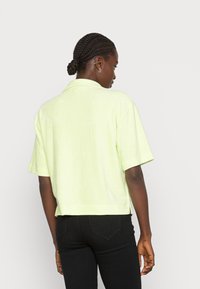 Polo de manga curta, em verde claro, com um acabamento texturizado, apresentando colarinho e um design ligeiramente encurtado na parte de trás.
